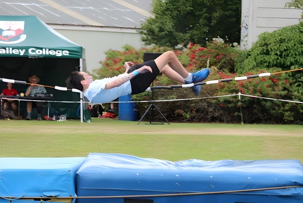 Eine Schülerin des Kaikorai Valley College führt einen Hochsprung auf einem Grasfeld vor dem College-Banner aus.