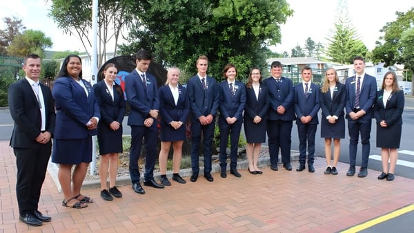 Eine Gruppe von Schülerinnen und Schülern des Kaipara College steht auf einem gepflasterten Außenbereich umgeben von Bäumen.