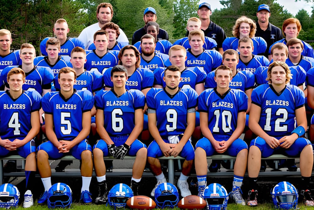 Eine Gruppe junger Football-Spieler der Kalkaska High School sitzt zusammen im Freien auf einer Grasfläche.