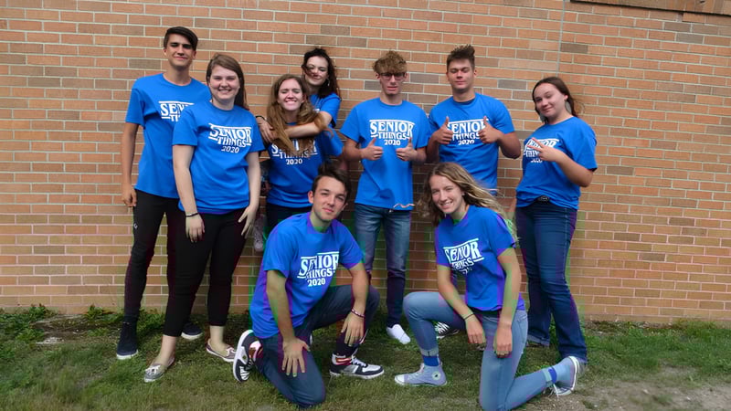Eine Gruppe Schüler der Kalkaska High School steht vor einer Backsteinmauer und trägt einheitliche blaue T-Shirts.