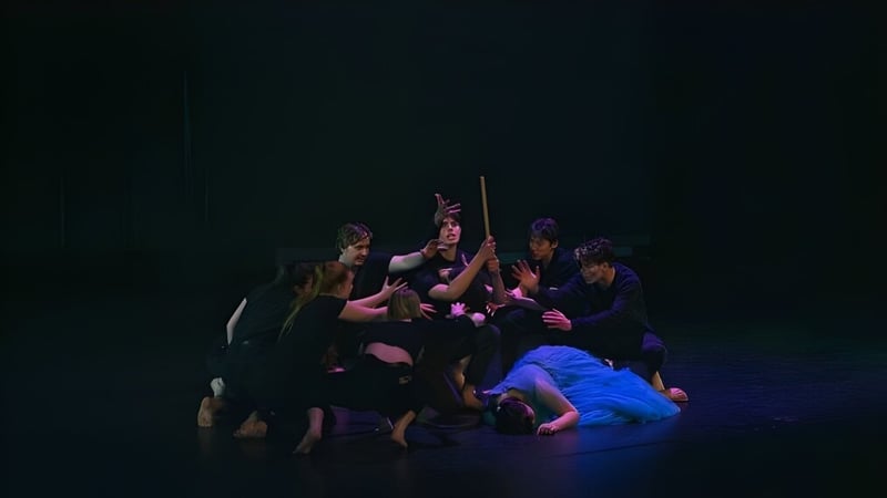 Eine Gruppe von Schülerinnen und Schülern der Kamo High School steht auf einer dunklen Bühne, während eine Person in blauer Kleidung im Mittelpunkt steht.