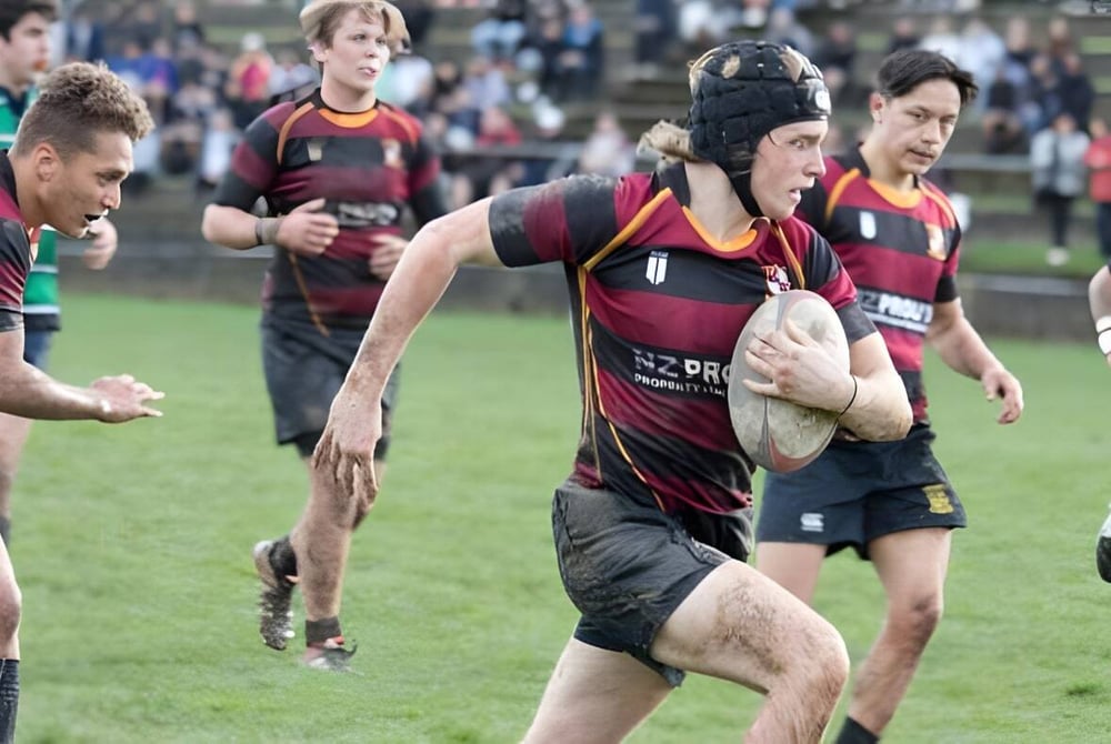 Eine Gruppe von Rugbyspielern des Kapiti College spielt ein intensives Match auf einem Grasfeld mit Zuschauern im Hintergrund.