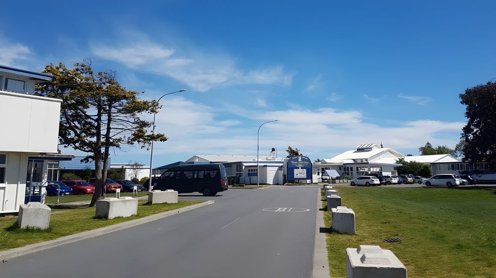 Ein gepflasterter Weg führt durch eine Grünfläche auf dem Campus des Kapiti College mit mehreren Gebäuden im Hintergrund.