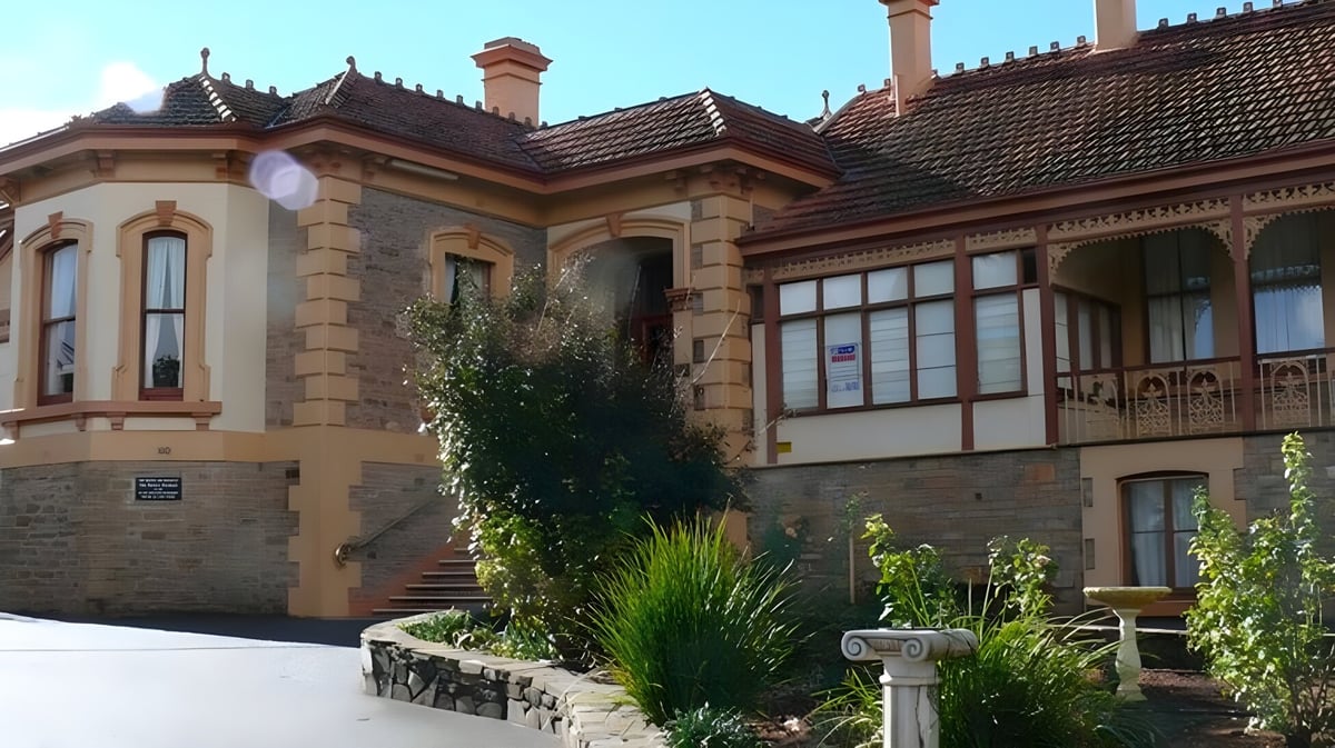 Das historische Hauptgebäude der Kapunda High School mit einem Garten im Vordergrund unter blauem Himmel.