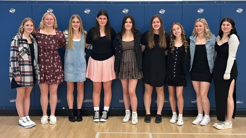 Eine Gruppe Schülerinnen steht vor einem blauen Hintergrund mit weißen Scheinwerfern auf dem Campus der Kate Andrews High School.