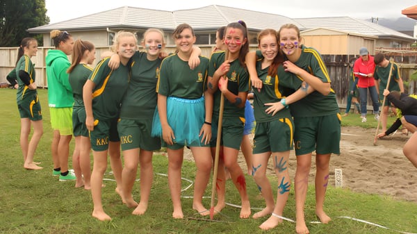 Eine Gruppe junger Athletinnen des Katikati College steht auf einem Grasfeld vor einem Wohngebäude.