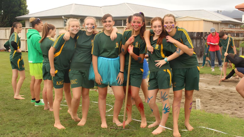 Eine Gruppe junger Athletinnen des Katikati College steht auf einem Grasfeld vor einem Wohngebäude.