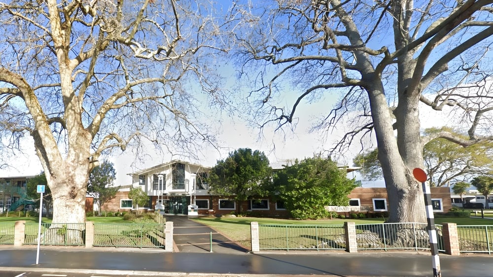 Das historische Gebäude von Katikati College ist von einem von Bäumen gesäumten Gelände und einem schmiedeeisernen Zaun umgeben.