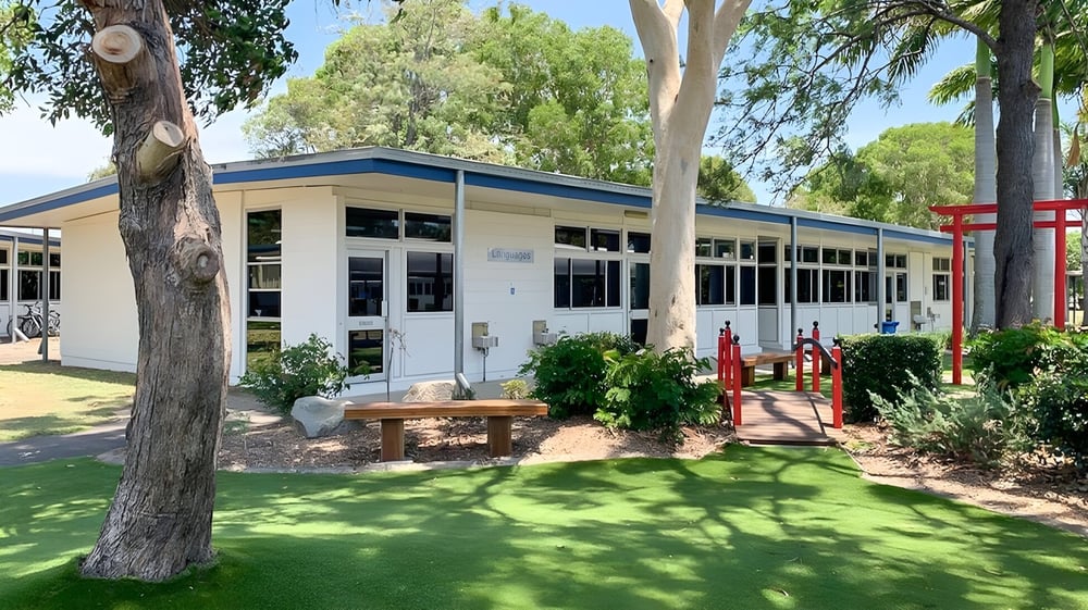 Das moderne einstöckige Gebäude auf dem Campus des Kawana Waters State College ist von Grünflächen und großen Bäumen umgeben.