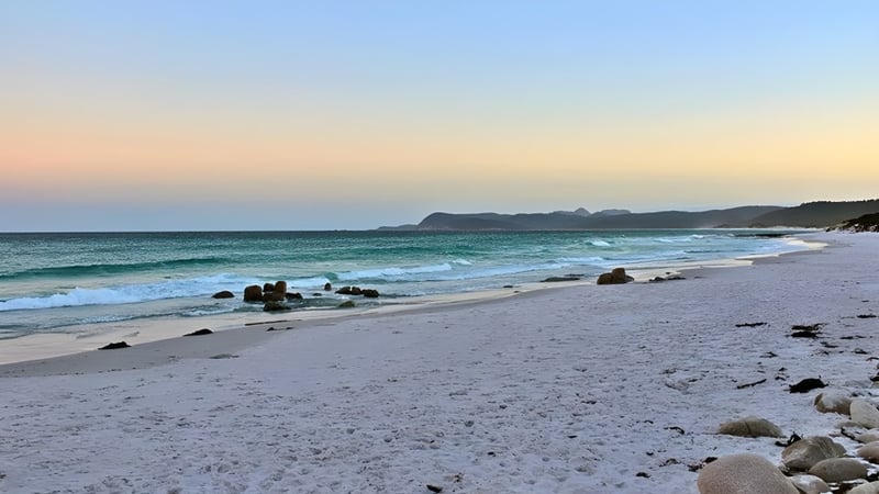 Ein ruhiger Strand mit Wellen und Felsen unter dem Himmel bei Tageswechsel in der Umgebung vom Kawana Waters State College.