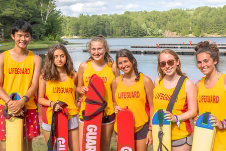Eine Gruppe von Rettungsschwimmern steht am See auf dem Campus der Kedron State High School vor grünen Bäumen.