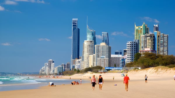 Menschen spazieren an einem sonnigen Strand mit moderner Skyline im Hintergrund nahe der Keebra Park State High School.