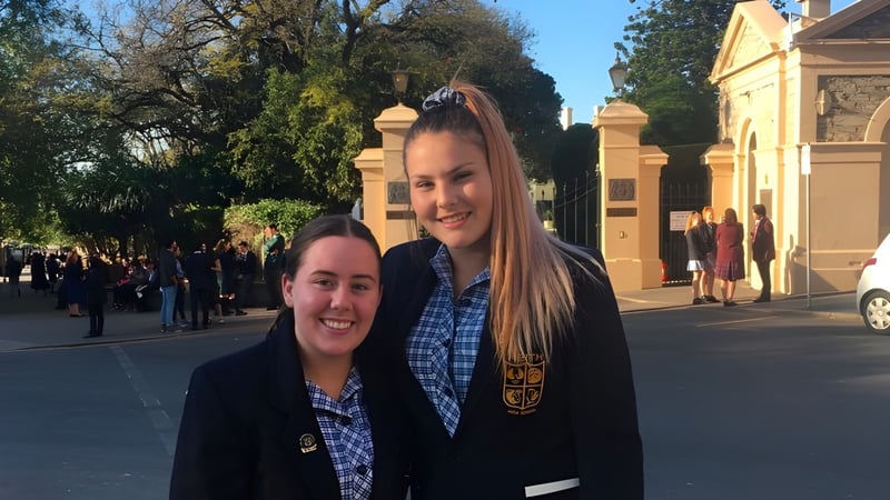 Zwei Schülerinnen stehen lächelnd vor einem historischen Gebäude auf dem Gelände der Keith Area School.