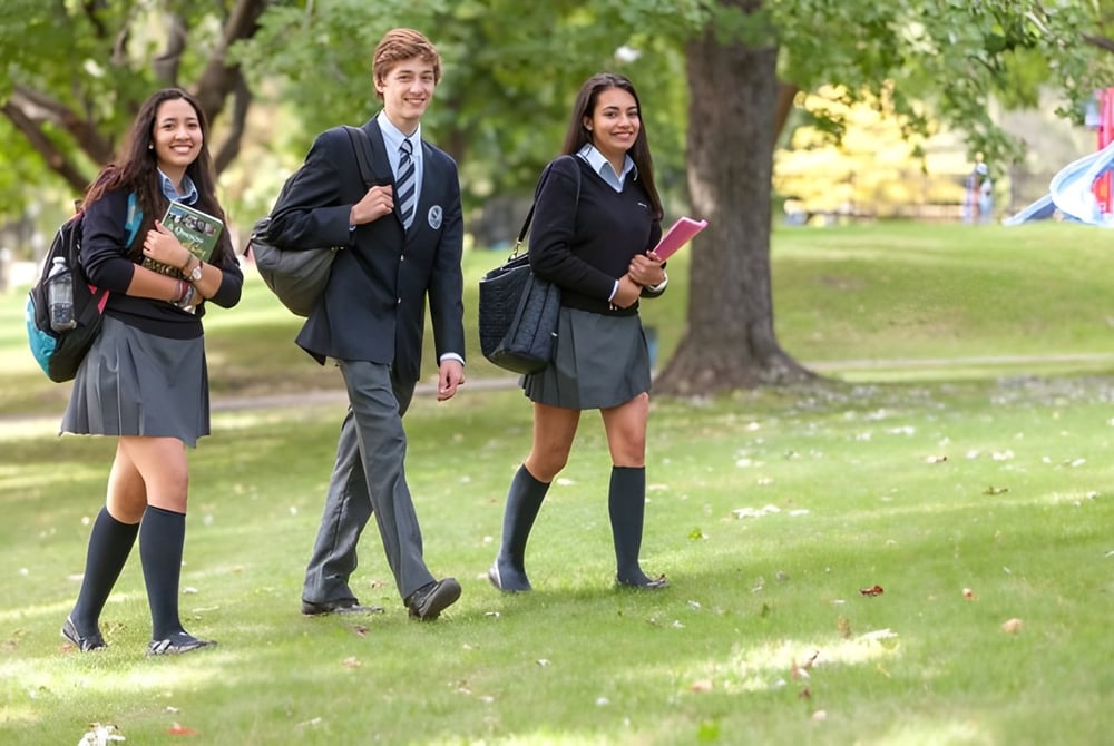 Drei Schülerinnen und Schüler der Kells Academy gehen auf einem grasbewachsenen Weg umgeben von Bäumen.