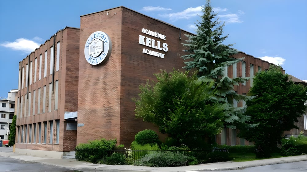 Das große Backsteingebäude mit Uhrenturm auf dem Campus der Kells Academy ist von Bäumen und Grün umgeben.