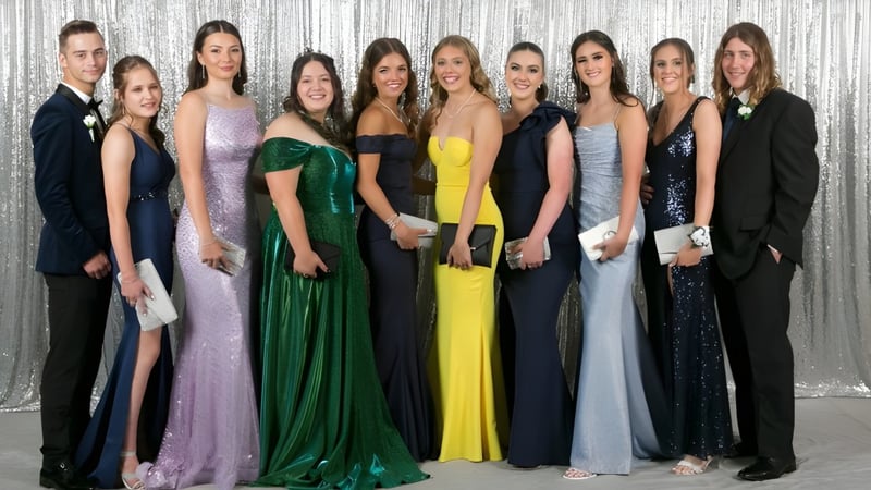 Eine Gruppe elegant gekleideter Personen posiert vor einem silbernen Hintergrund auf dem Campus der Kelmscott Senior High School.