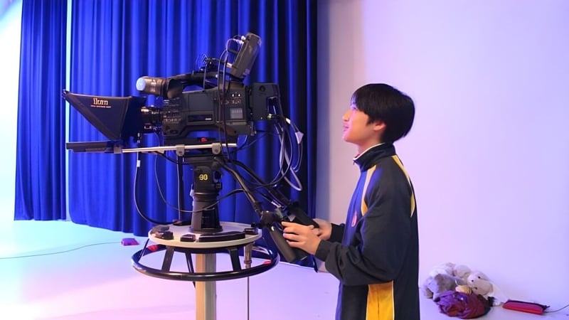 Ein Schüler der Kelmscott Senior High School steht vor einer großen Videokamera mit blauem Vorhang als Hintergrund.