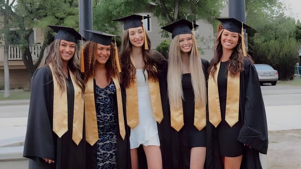 Fünf Schülerinnen der Kelowna Secondary School stehen im Freien in ihren Abschlussroben vor einem Schulgebäude.