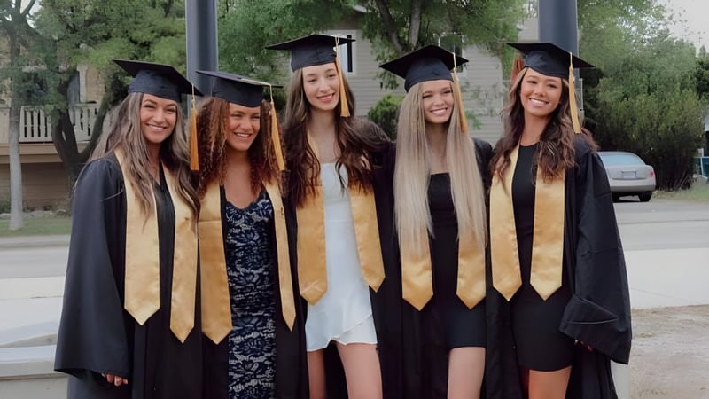 Fünf Schülerinnen der Kelowna Secondary School stehen im Freien in ihren Abschlussroben vor einem Schulgebäude.