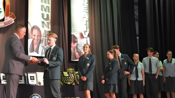 Schüler des Kelvin Grove State College erhalten auf der Bühne eine Auszeichnung von einem Mann im Anzug.