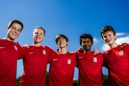 Eine Gruppe von fünf Schülern in roten Fußballtrikots steht vor blauem Himmel auf dem Campus des Kelvin Grove State College.