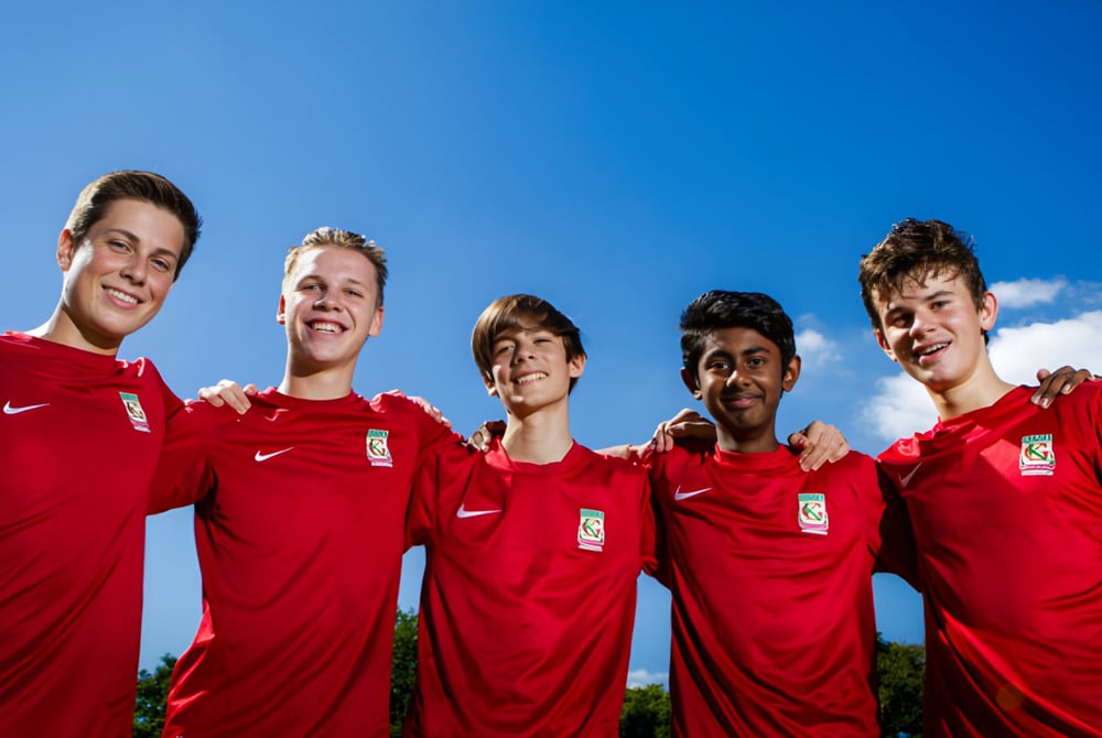 Eine Gruppe von fünf Schülern in roten Fußballtrikots steht vor blauem Himmel auf dem Campus des Kelvin Grove State College.