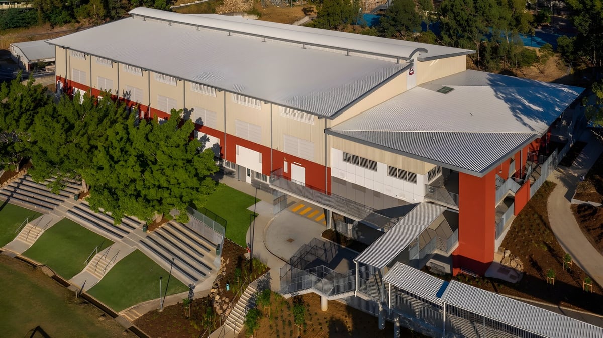Das moderne Industriegebäude des Kelvin Grove State College steht auf einem grasbewachsenen Hügel mit umgebendem Grün und blauem Himmel.
