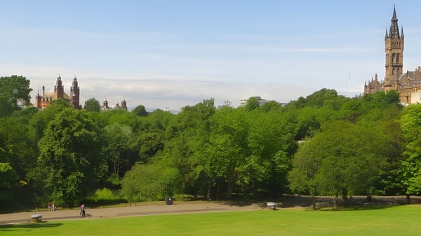 Menschen spazieren durch einen grünen Park mit Bäumen und einer historischen Kathedrale im Hintergrund am Kelvin Grove State College.