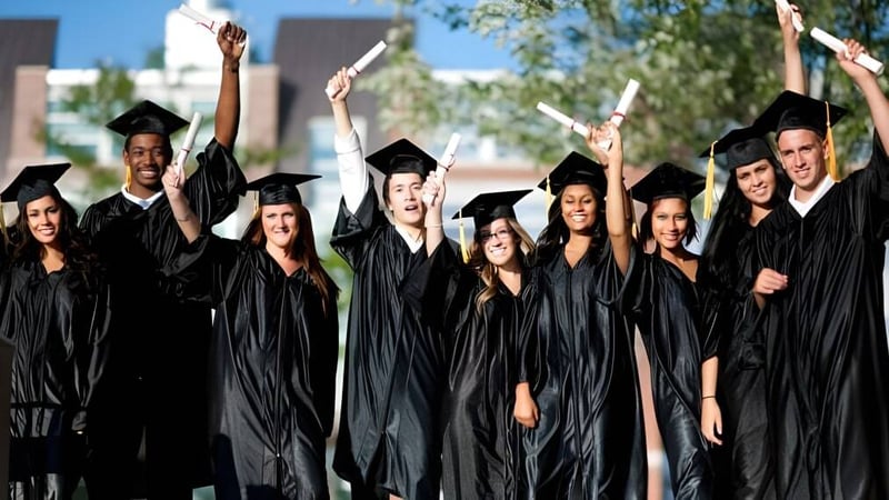 Eine Gruppe von Absolventen feiert ihre Abschlussfeier auf dem Gelände der Kelvin High School vor Bäumen und Gebäuden.