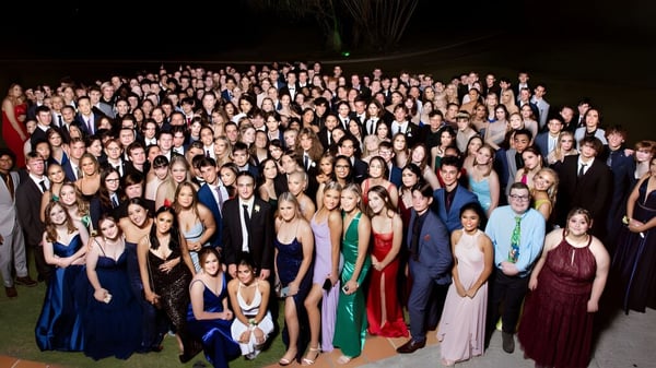 Eine Gruppe von Personen in formeller Kleidung bei einer Feier mit Feuerwerk im Hintergrund auf dem Campus der Kenmore State High School.