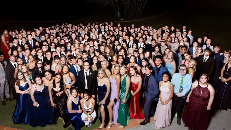 Eine Gruppe von Personen in formeller Kleidung bei einer Feier mit Feuerwerk im Hintergrund auf dem Campus der Kenmore State High School.