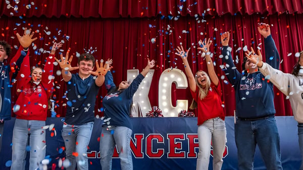 Eine Gruppe von Schülerinnen und Schülern der Kennedy Catholic High School feiert vor einem großen NCEF-Schild mit roten Vorhängen im Hintergrund.