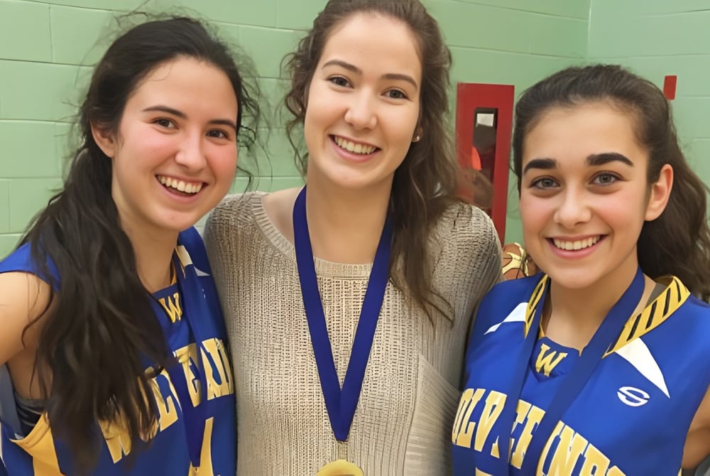 Drei Schülerinnen in blauen Sportuniformen posieren vor einer grünen Wand auf dem Gelände der Kensington Intermediate Senior High School.