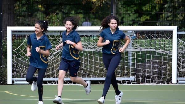 Drei Schülerinnen der Kensington Park School laufen auf dem Sportfeld vor einem Torpfosten.