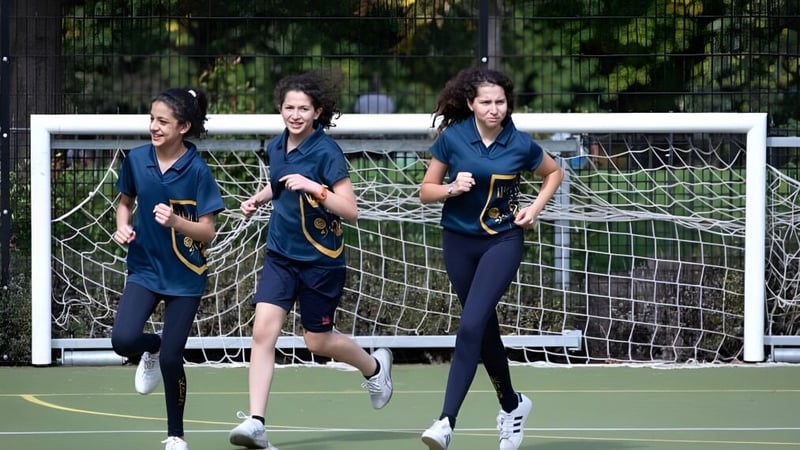 Drei Schülerinnen der Kensington Park School laufen auf dem Sportfeld vor einem Torpfosten.