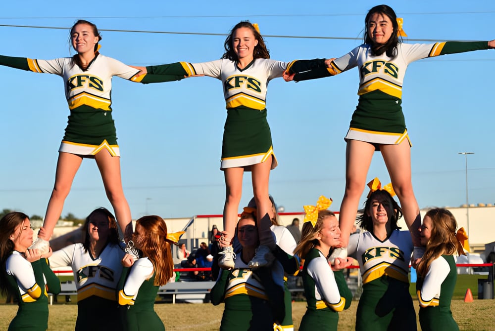 Schülerinnen und Schüler der Kenston Forest School führen auf dem Sportfeld einen Cheerleading-Stunt unter klarem Himmel aus.