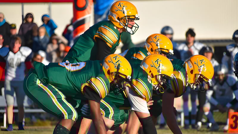 Eine Gruppe von Fußballspielern in grünen und gelben Trikots steht auf dem Spielfeld der Kenston Forest School mit Zuschauern im Hintergrund.