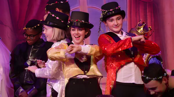 Eine Gruppe Schülerinnen und Schüler des Kent College stehen in bunten Kostümen auf einer Bühne vor einem roten Vorhang.