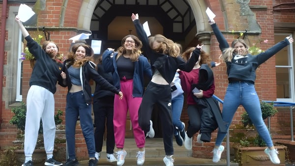 Eine Gruppe Schülerinnen des Kent College Pembury verlässt jubelnd ein Backsteingebäude.