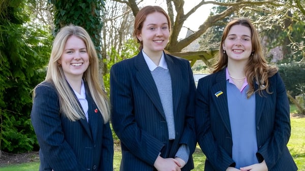 Drei Schülerinnen in Schuluniformen des Kent College Pembury stehen zusammen und lächeln im Wald.