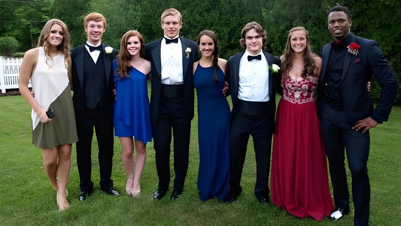 Eine Gruppe Schüler der Kent School steht in formeller Kleidung zusammen auf einer Wiese vor einem weißen Lattenzaun.