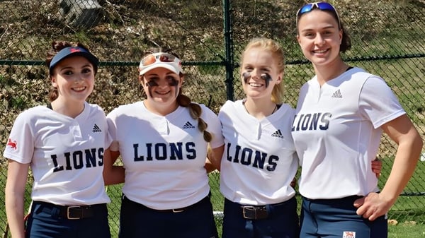 Vier Schülerinnen tragen weiße Shirts mit Lions-Logo und stehen auf dem Sportplatz der Kent School.