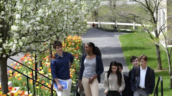 Eine Gruppe Schüler der Kent School geht auf einem Weg entlang blühender Bäume und bunter Blumen.