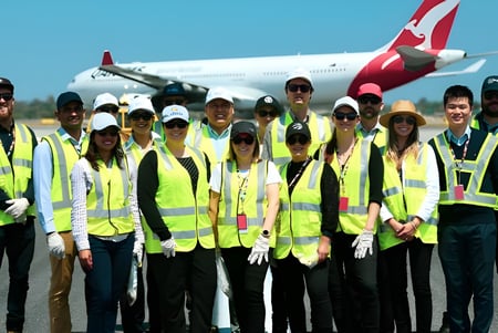Schüler der Kent Street Senior High School tragen auf dem Rollfeld gelbe Sicherheitswesten vor einem großen Passagierflugzeug.