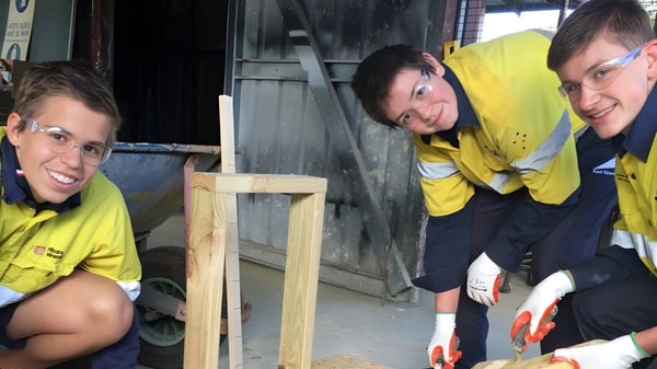 Drei Schülerinnen und Schüler der Kent Street Senior High School arbeiten gemeinsam auf einer Baustelle mit Werkzeugen und Baumaterialien.