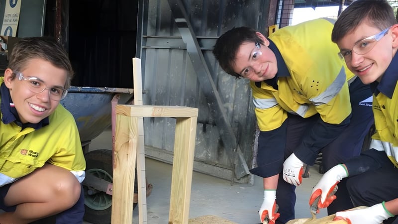 Drei Schülerinnen und Schüler der Kent Street Senior High School arbeiten gemeinsam auf einer Baustelle mit Werkzeugen und Baumaterialien.