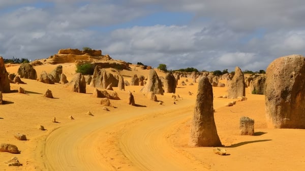 Eine weite Wüstenlandschaft mit hohen Felsformationen und einem gewundenen Pfad unter bewölktem Himmel.