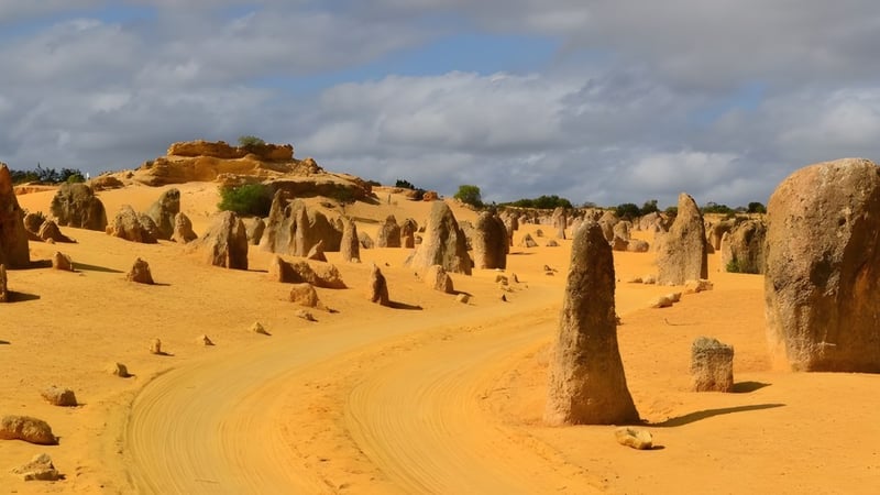 Eine weite Wüstenlandschaft mit hohen Felsformationen und einem gewundenen Pfad unter bewölktem Himmel.