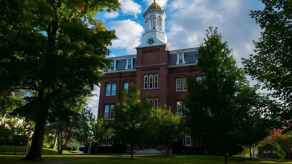 Das Backsteingebäude der Kents Hill School mit hohem weißem Turm steht umgeben von Bäumen und Grünflächen.
