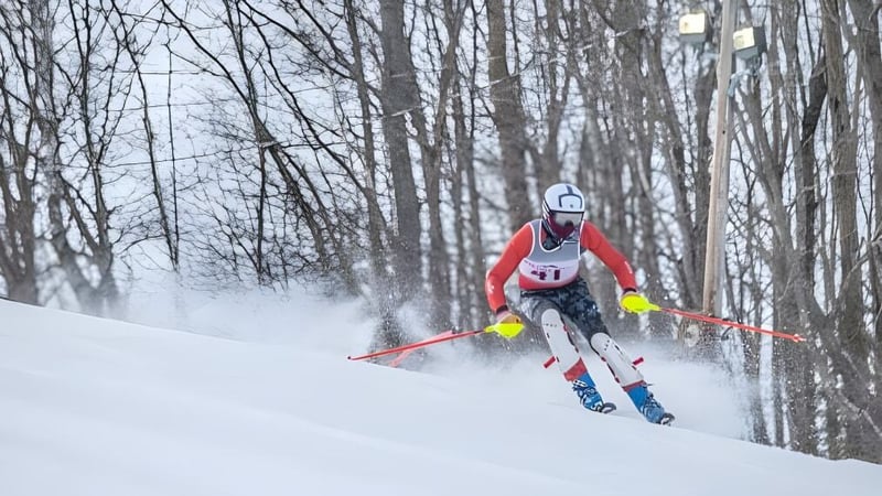 Ein Skifahrer in roter Jacke fährt einen schneebedeckten Hang am Wald auf dem Gelände der Kents Hill School hinunter.